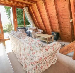 A living room with floral sofas a wooden coffee table and wooden walls at Apple Tree Lodge in Gillingham