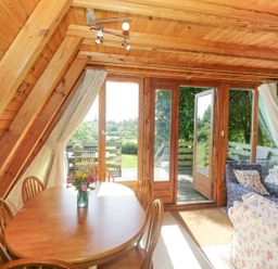 A wooden interior room with a dining table and chairs and a seating area with sofas near glass doors leading outside at Apple Tree Lodge in Gillingham