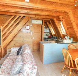 A wooden cabin interior with a floral sofa a small dining table with chairs a kitchen counter and skylight windows at Apple Tree Lodge in Gillingham