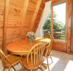 A dining area with a wooden table and chairs next to large windows overlooking a garden at Apple Tree Lodge in Gillingham
