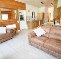 A living area with two brown sofas a wooden dining table and an open kitchen at Kipling Lodge in Rudyard