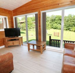 A living room with large windows brown leather sofas wooden table and television at Kipling Lodge in Rudyard