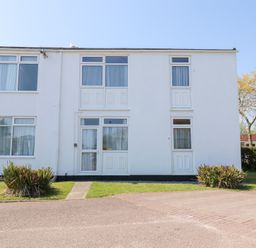 A white two-story building with multiple windows and doors surrounded by grass and plants at La Capsule in Dawlish Warren