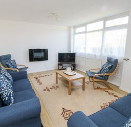 A living room with blue sofas and armchairs around a wooden coffee table near a television at La Capsule in Dawlish Warren