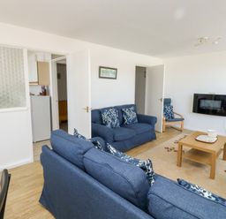 A living room with blue sofas a wooden coffee table and a wall-mounted television at La Capsule in Dawlish Warren