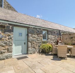 An outdoor patio with stone walls a light blue door and a table with four wicker chairs at Cornel Glyd in Talybont near Barmouth