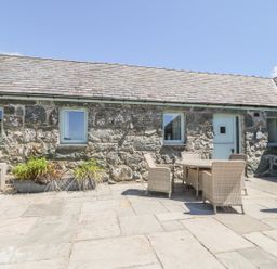 An outdoor patio area with stone flooring stone walls a table with four wicker chairs and potted plants at Sisial-y-Mor in Talybont near Barmouth