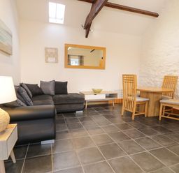 A living room with a black sofa wooden dining table with chairs a coffee table a lamp and a wall mirror at Sisial-y-Mor in Talybont near Barmouth