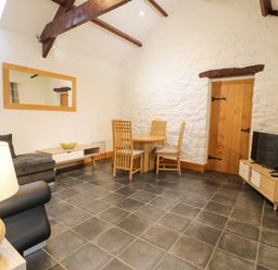 A living room with a dining table and chairs a sofa a television on a stand and a large mirror on the wall at Sisial-y-Mor in Talybont near Barmouth