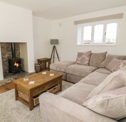 A living room with a beige sectional sofa wooden coffee table and a wood burning stove at 1 Dunkirk Cottages Humshaugh near Hexham