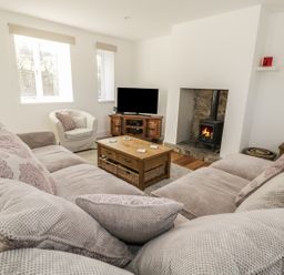 A living room with a large sectional sofa a white armchair a wooden coffee table a television on a wooden stand and a fireplace at 1 Dunkirk Cottages in Humshaugh near Hexham