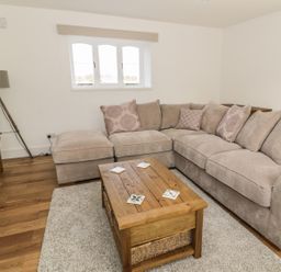 A living room with a large beige sectional sofa cushions wooden coffee table and tripod floor lamp at 1 Dunkirk Cottages in Humshaugh near Hexham