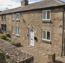 Exterior view of a stone cottage with white door and windows and a gravel pathway at 1 Dunkirk Cottages Humshaugh near Hexham