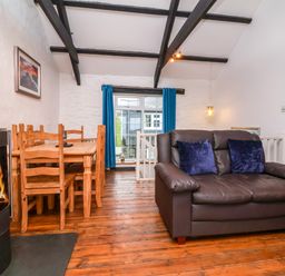 A living room with wooden dining table and chairs a brown leather sofa with blue cushions and a fireplace at Threshings Cottage in Tintagel