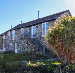 Stone building with external metal staircase and palm tree in front at Threshings Cottage in Tintagel