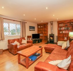A living room with leather sofas a wooden coffee table bookshelves and a fireplace at Fig Tree Cottage in Bickleigh