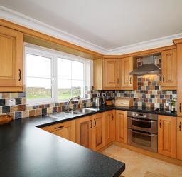 A kitchen with wooden cabinets black countertops a stainless steel oven and a window overlooking a stone wall at Benbulben View in Tullaghan County Leitrim