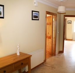 A hallway with a wooden console table with a lamp and sculpture two framed pictures on the wall and wooden doors at Benbulben View in Tullaghan County Leitrim