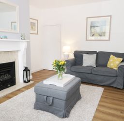 A living room with a grey sofa yellow flowers on a grey ottoman and a fireplace at Rose Cottage in Lesbury near Alnmouth