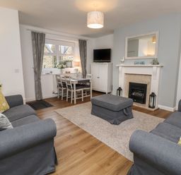 A living room with two sofas a fireplace a dining table and a television at Rose Cottage in Lesbury near Alnmouth