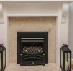 A fireplace with black metal grate and stones inside flanked by two black lanterns with candles at Rose Cottage Lesbury near Alnmouth