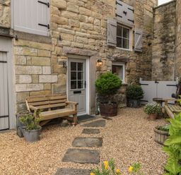 An outdoor courtyard with stone walls wooden benches potted plants and a gravel walkway at The Olde Stables in Warkworth