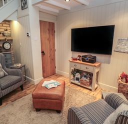 A living room with armchairs ottoman and television on wall at The Olde Stables in Warkworth