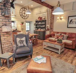 A living room with a leather sofa striped armchairs a coffee table and kitchen area at The Olde Stables in Warkworth