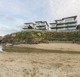 Modern apartment buildings on a cliff above a sandy beach with a small water pool at Chapel Rock View The Dunes in Perranporth
