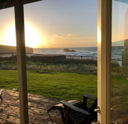 A view of a lawn and ocean with chairs on a patio at Chapel Rock View The Dunes in Perranporth