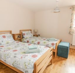 A bedroom with two single beds with floral bedding a small shelving unit and a turquoise ottoman at The Stable at Church Farm House Limpenhoe near Reedham