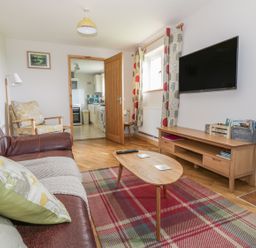 A living room with a brown leather sofa a wooden coffee table a wall-mounted television and a wooden TV stand at The Stable at Church Farm House Limpenhoe near Reedham