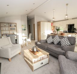 A living room with sofas and a coffee table next to a dining area and kitchen at Woodstock Lodge in Wemyss Bay