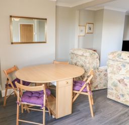 A dining area with a wooden table and folding chairs with purple cushions next to floral armchairs at 27 Whitegates in Ludham