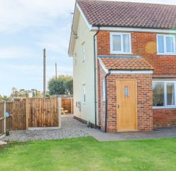 A backyard with grass a wooden fence and a brick house with a wooden door at 27 Whitegates in Ludham