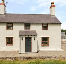 A two story house with white walls and a dark door in a rural setting at Pen Y Bryn Cottage in Llandudno
