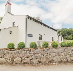 A white house with a stone wall and shrubs outside at Pen Y Bryn Cottage in Llandudno