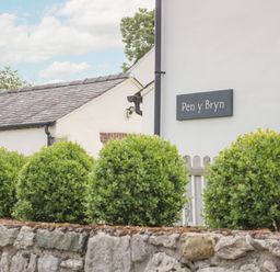 Green bushes along a stone wall outside a white building with a sign that reads Pen y Bryn in Llandudno