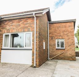 The exterior of a brick building with two windows concrete driveway and a grassy area with trees at Blaenywawr Annexe in Lampeter