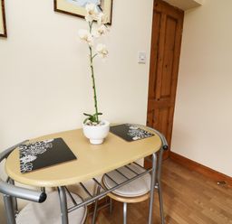 A small wooden table with two stools and a potted white orchid on top at Blaenywawr Annexe in Lampeter
