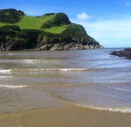 A coastal scene with rocky cliffs and green grass beside the sea at Martin Cottage in Ilfracombe