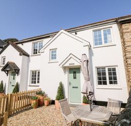 A white two-story cottage with green doors and potted plants outside a wooden fence at Martin Cottage in Ilfracombe