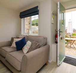 A living room with a sofa near a window and an open door leading to an outdoor seating area at Martin Cottage in Ilfracombe