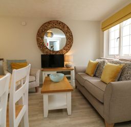 A living room with a sofa and armchair a coffee table a TV and a round mirror at Swallow Cottage in Ilfracombe