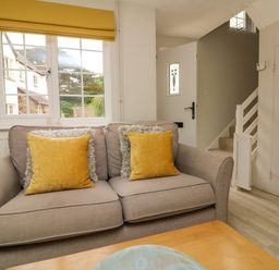 A living room with a beige sofa with yellow cushions near a window and a white door at Swallow Cottage in Ilfracombe