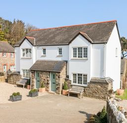 The exterior of a white and stone two story house with two green front doors and benches outside at Kingfisher Cottage in Ilfracombe