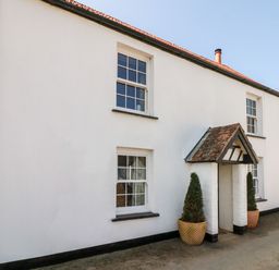 The exterior of a white two-story house with four windows a small porch and two potted plants on a driveway at Partridge Cottage in Ilfracombe