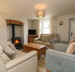 A living room with couches a wooden coffee table a wood burning stove and a television at Partridge Cottage in Ilfracombe