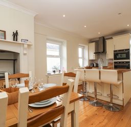 A dining table set with plates and glasses next to a kitchen island with stools in a kitchen at Pound Rocks in Tintagel
