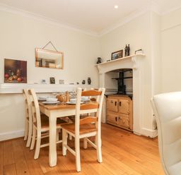 A dining area with a wooden table set for six chairs and a vintage stove in a corner at Pound Rocks in Tintagel